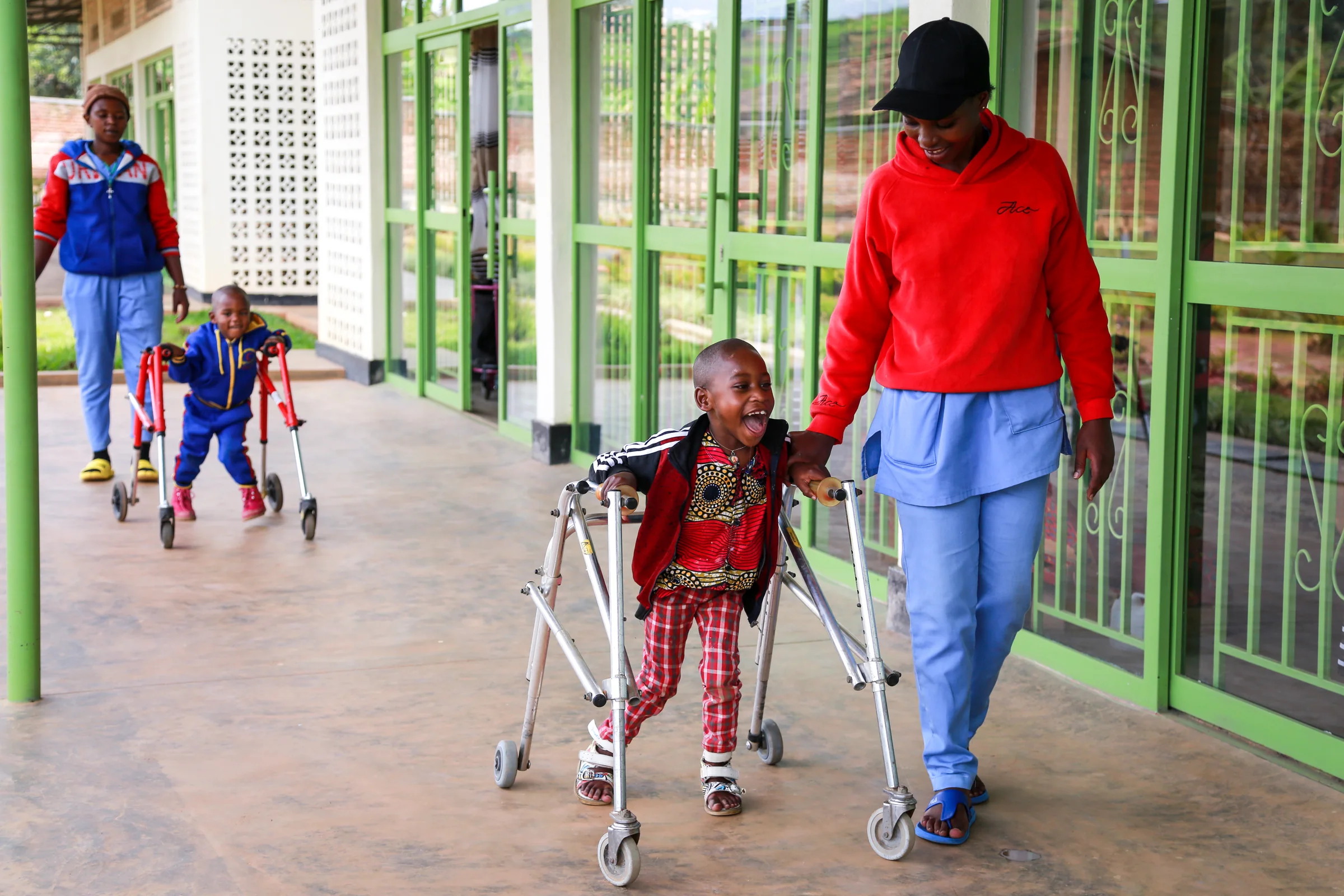 Therapists accompany two children using mobility walkers along the ASFA rehabilitation center walkway in Rwanda