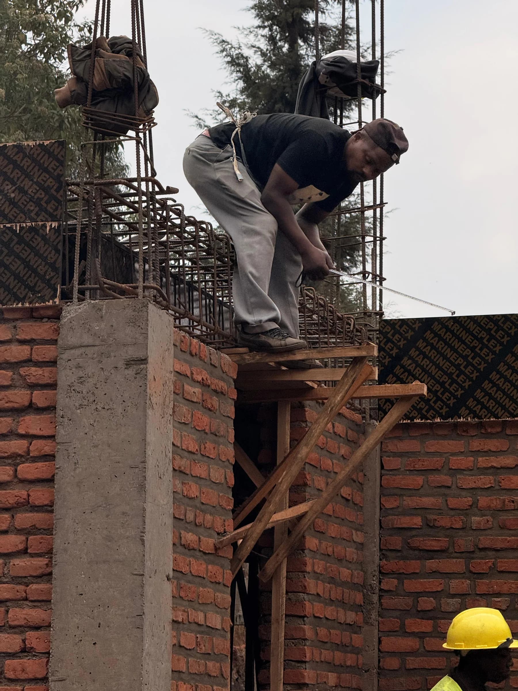 A builder checks dimensions where new masonry meets the reinforced-concrete frame at Sunzu