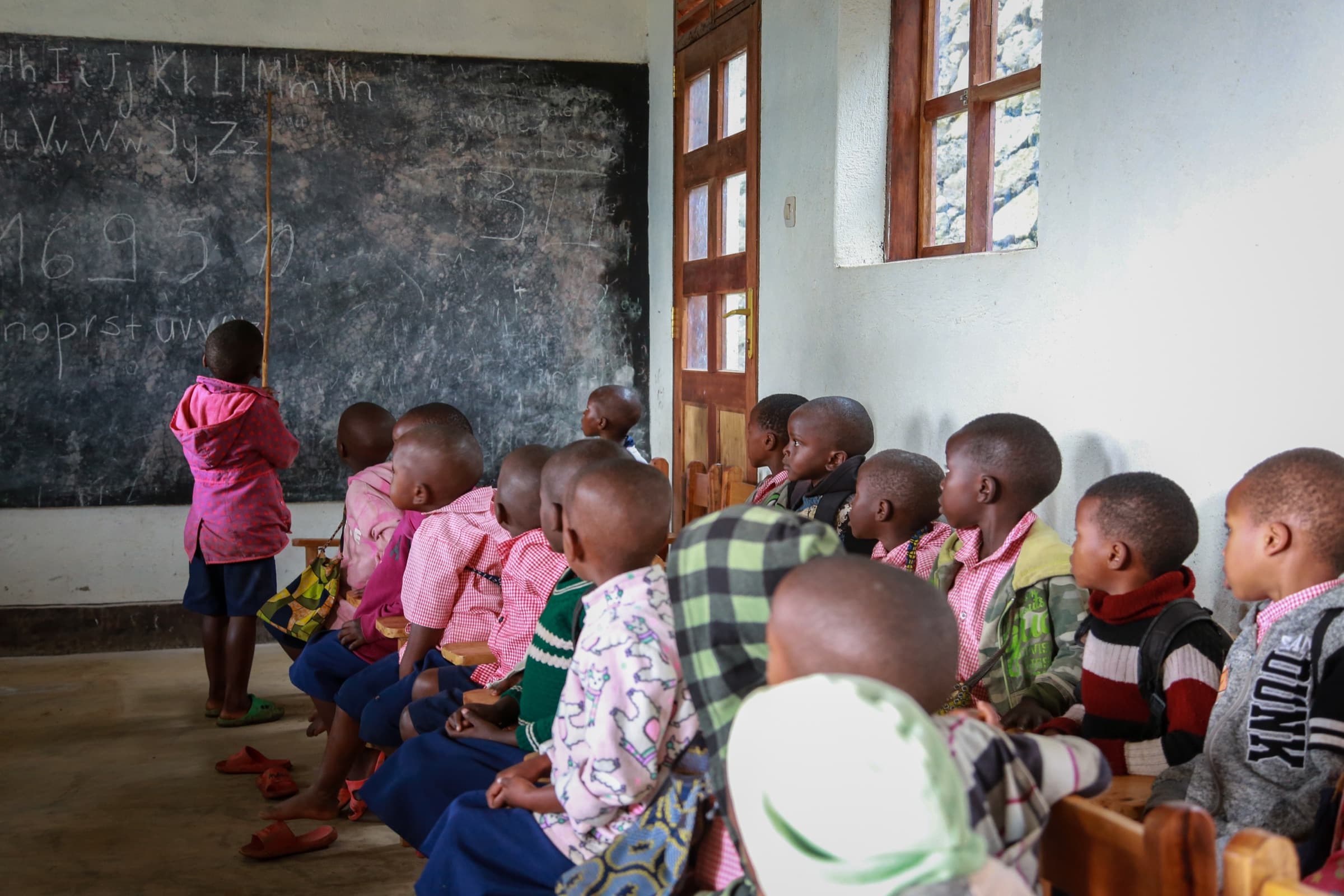 Children watching a classmate work at the blackboard inside the Sunzu Village library